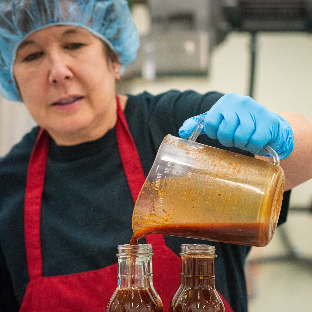 Production worker pouring sauce into bottles