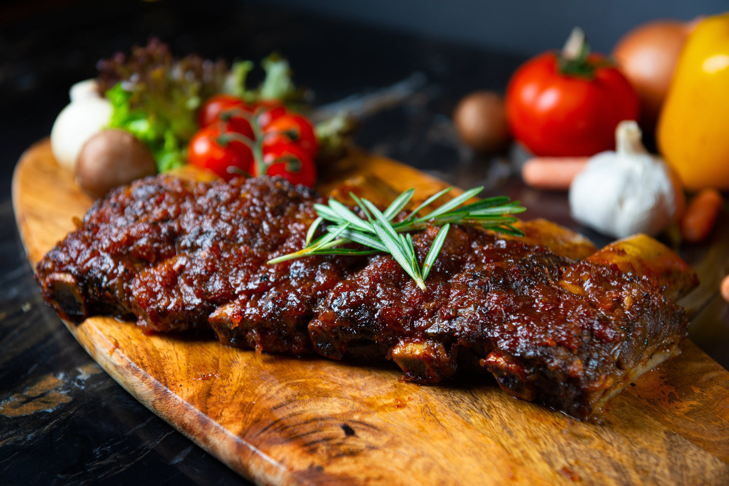 Rack of ribs on a cutting board with fresh veggies in the background