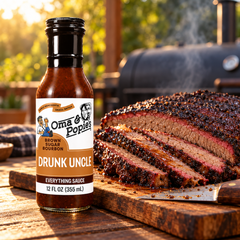 Oma & Popie's Drunk Uncle sauce bottle next to a sliced brisket on a wooden board with a smoker in the background